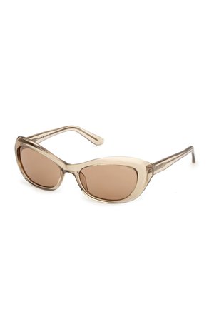 Przezroczyste beżowe okulary przeciwsłoneczne w kształcie kocich oczu z brązowymi przyciemnianymi soczewkami i cienkimi zausznikami, leżące płasko na białej powierzchni.