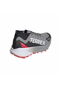 Baskets de sport grises avec une tige noire, grand logo "TERREX" blanc, semelle intermédiaire argentée et semelle extérieure rouge avec des crampons de traction.