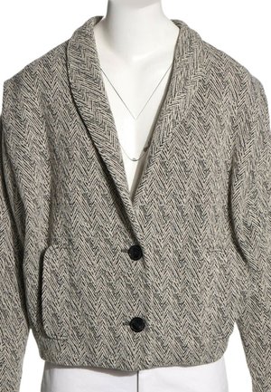 Blazer court à motif chevrons gris et noir, avec larges revers et deux boutons noirs à l'avant, présenté sur un mannequin blanc.