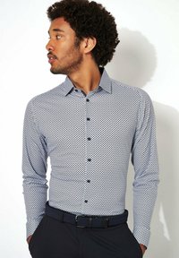 Marineblauwe en witte overhemd met lange mouwen en een klein stippenpatroon, knoopsluiting aan de voorkant en contrasterende kraag; gedragen met een zwarte riem en broek.