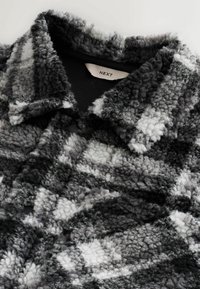 Texturierte schwarz-graue kariert Jacke aus weichem, flauschigem Material mit scharfem Kragen und sichtbaren Nähdetails. Markenetikett ist enthalten.