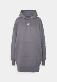 Överdimensionerad grå hoodie i mjukt material, med en framficka, snörning i huvan och vit textdetalj längs en ärm.