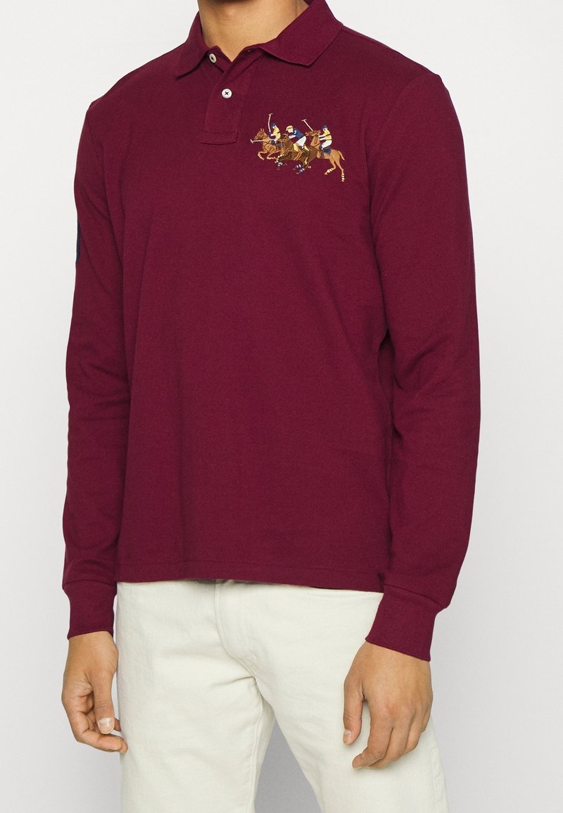 Burgunder långärmad polo skjorta i bomull. Har en brodyr av en ryttare på vänster bröst och en krage med knappar och en strukturerad yta.