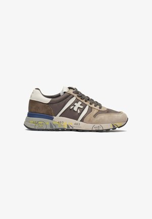 Sneakers feature a mix of brown suede and leather, white accents, lace-up design, and a patterned outsole with yellow and gray details.