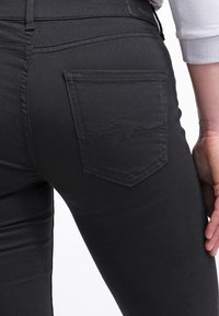 Vaqueros de mezclilla negra con un bolsillo trasero que presenta un sutil diseño de costura, forma ajustada y textura suave.