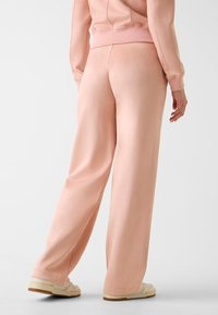Pantaloni della tuta color rosa chiaro a gamba larga, realizzati in tessuto morbido. Presentano una texture liscia e una cintura elastica. Abbinati a sneaker color crema.