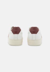 White leather sneakers with maroon accents, rounded shape, textured rubber sole, and stitching details; logo embossed on back.