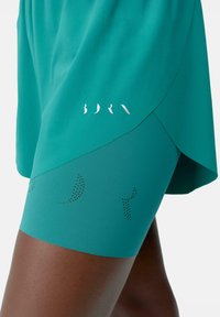 Turquoise athletic shorts with a semi-transparent overlay. Features perforated patterns and a reflective logo accent near the hem.