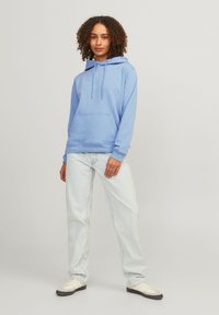 Light blue hoodie with a kangaroo pocket, drawstring hood, and ribbed cuffs, paired with light-wash jeans and low-top sneakers.