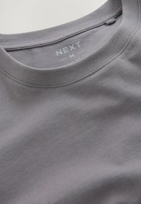 Grå t-shirt med kort ärm och rund halsringning. Tillverkad av mjukt, stretchigt material. Har en etikett med "NEXT" och storlek "M" inuti kragen.