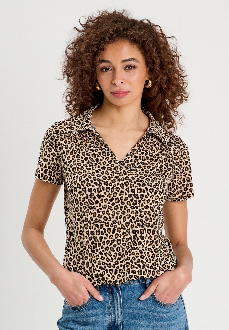 Chemise à manches courtes en imprimé léopard beige et noire, avec un col et une coupe décontractée, associée à un jean en denim. Texture douce.