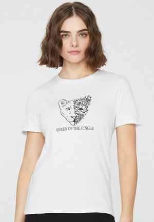 Kobieta w białej koszulce z grafiką przedstawiającą pół twarzy lwa i pół kwiatowego wzoru, poniżej napis "KRÓLOWA DŻUNGLI"