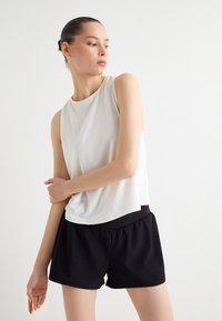 Top blanco sin mangas con una textura suave y escote redondeado, combinado con pantalones cortos negros elásticos que cuentan con una cinturilla elástica.