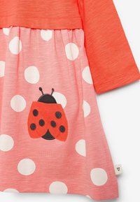 Haut corail à manches longues, associé à une jupe rose à pois blancs avec une application de coccinelle rouge et noire à la taille.