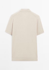 Beige ribstrikket poloshirt med kort krave, korte ærmer og lige kant. Stoffet virker blødt og tekstureret.