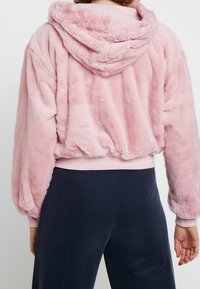 Rosa fuskpäls hoodie med huva, elastisk nederkant och ärmslut. Mjuk-textur med en avslappnad passform, minimal sömdetaljering på baksidan.