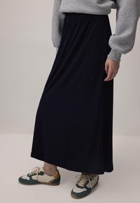 Gonna lunga con elastico in vita di colore navy, realizzata in tessuto morbido, abbinata a sneakers casual multicolori, vista di lato.