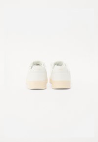 White leather sneakers with a smooth finish, featuring a beige rubber sole and embossed branding on the heel and side.