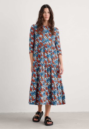 Bloemen midi-jurk met blauwe basis, versierd met rode en witte bloemen, driekwart mouwen en een gelaagde rok. Gemaakt in combinatie met zwarte plateau-sandalen.