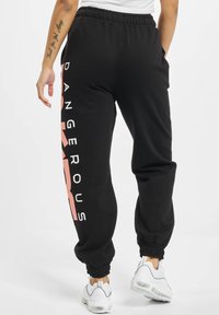 Black sweatpants with an elastic waistband and ankle cuffs. Features large "DANGEROUS" text in light pink along one side.