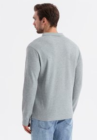 Grå långärmad polo med krage, mjuk textur och avslappnad passform, kombinerad med ljusblå denimjeans.