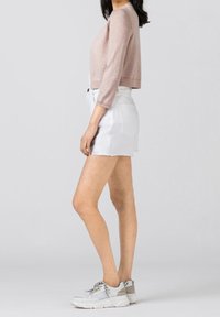 Maglione cropped rosa chiaro con maniche tre quarti, abbinato a pantaloni shorts in denim bianco con orlo sfilacciato, indossato con sneakers bianche chunky.