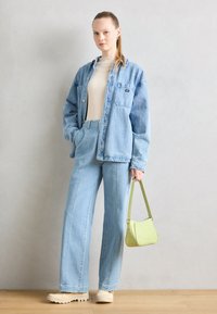 Chaqueta de mezclilla, suéter ligero de punto color crema, jeans de tiro alto azul claro, zapatos de plataforma beiges y un pequeño bolso cruzado verde.