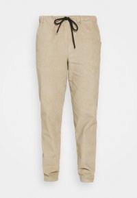 Bežové kordové kalhoty s elastickým pasem a zúženými nohavicemi, s ribovanou texturou a bez viditelných kapes nebo ozdob.