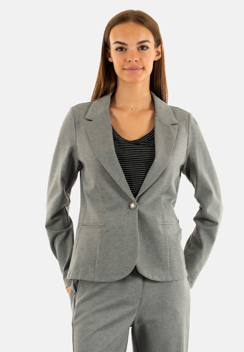 Blazer gris de tela suave con solapas de muesca, cierre de un solo botón y ajuste estructurado. Combinado con una blusa de rayas en blanco y negro.