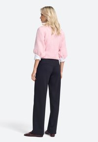 Suéter de punto rosa claro con mangas abullonadas, combinado con pantalones negros de cintura alta. El conjunto incluye zapatos marrones con cordones.