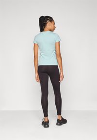 Lyseblå kortermet skjorte kombinert med svarte leggings og svarte treningssko. Har en tettsittende design og glatt stoffstruktur.