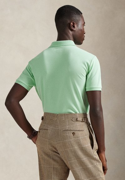 Πράσινο πουκάμισο πόλο με κλασικό γιακά, σε συνδυασμό με καφέ καρό παντελόνι με εφαρμοστή γραμμή και ορατά κουμπιά.