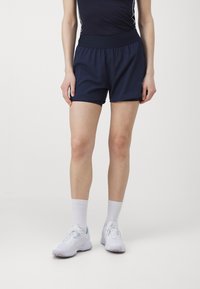 Bermudos deportivos azul marino con cinturilla elástica, fabricados con un tejido suave y ligero. Combinados con zapatillas deportivas blancas y calcetines.