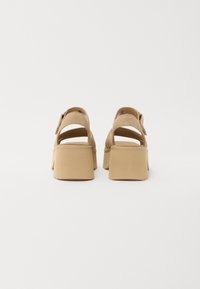 Beżowe sandały na platformie o gładkim, teksturowanym wykończeniu. Posiadają wiele pasków i masywny obcas zapewniający stabilność.