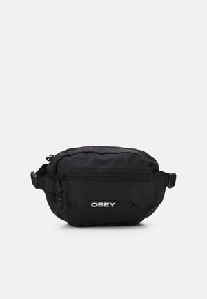 Musta nailoninen olkalaukku, jossa on vetoketjullinen pääosasto, etutasku, säädettävä olkahihna ja valkoinen "OBEY"-logopatch.