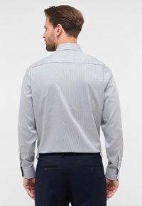 Camicia a maniche lunghe da uomo vista da dietro; presenta righe verticali blu e bianche, un colletto alto e polsini con bottoni. Il materiale sembra liscio.