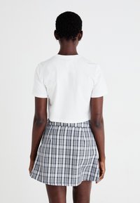 Camiseta blanca recortada combinada con una falda de cuadros de talle alto con patrones en gris, negro y blanco. Mangas cortas y diseño casual.