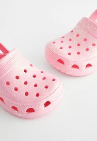 Rosafarbene Clogs aus leichtem Material, mit mehreren Belüftungslöchern, glatter Oberfläche mit Glitzereffekt und einem Fersenriemen.