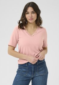 Top corto de manga corta ribeteado en rosa claro con escote en V y un delicado borde de encaje floral. Combinado con unos vaqueros de tiro alto, que muestran un ajuste relajado.