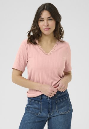 Světle růžový ribbed top s krátkým rukávem a výstřihem do V, který má květinovou krajkovou lemovku. Nosený s modrými džíny s vysokým pasem, které ukazují uvolněný střih.