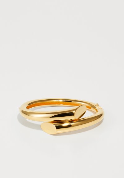 Armbanduhr aus goldfarbenem Metall mit einer glatten, glänzenden Oberfläche; verfügt über eine gebogene Form und zwei Enden mit abgerundeten Spitzen.