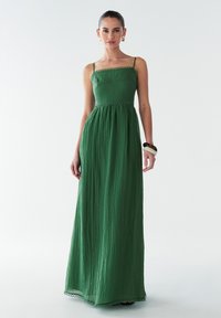 Grünes Maxikleid aus strukturiertem Stoff, mit verstellbaren Spaghetti-Trägern und tailliertem Oberteil. Verfügt über einen gewellten Saum an der Taille.