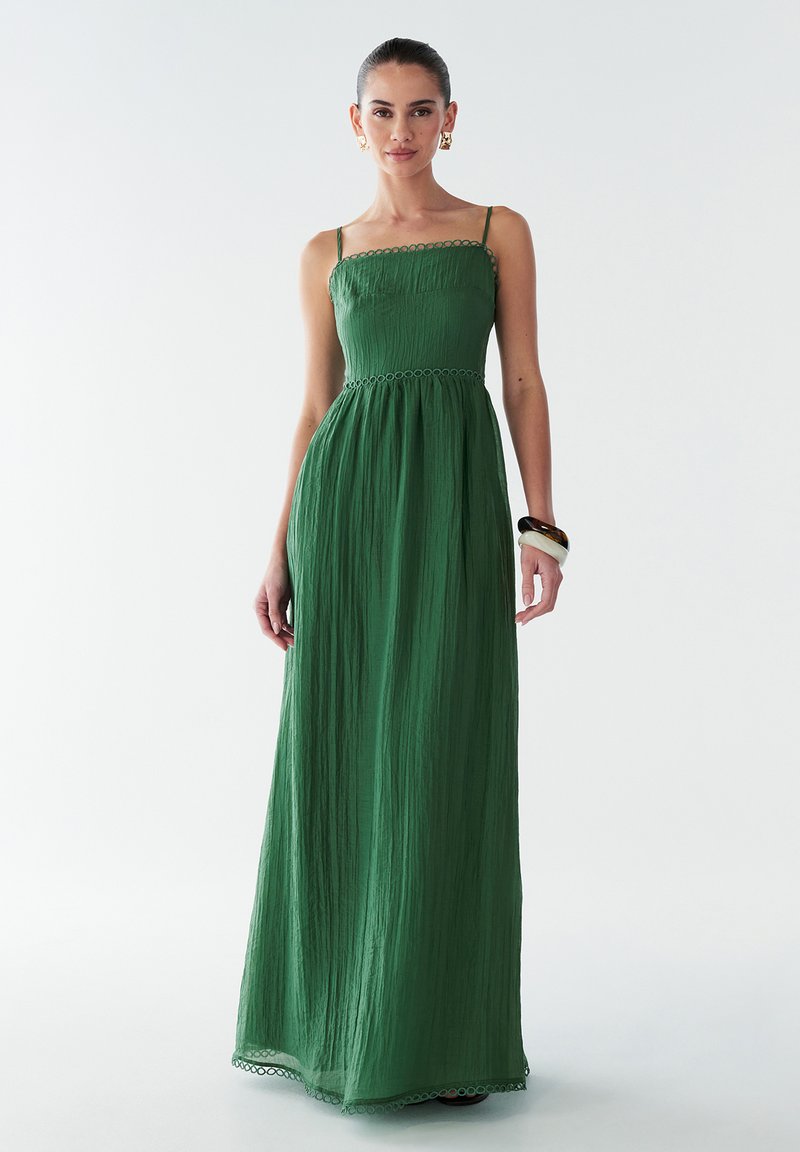 Grünes Maxikleid aus strukturiertem Stoff, mit verstellbaren Spaghetti-Trägern und tailliertem Oberteil. Verfügt über einen gewellten Saum an der Taille.