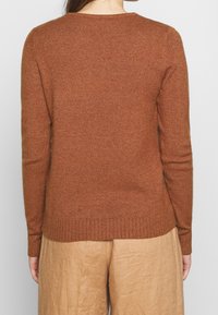 Brun tröja med ribbad krage och manschetter, mjuk textur, figursydd passform och lager på lager- fåll, kombinerad med ljusbeige vida byxor.