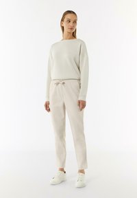 Hellgrau, Langarm-Sweatshirt, kombiniert mit beigen Jogginghosen mit elastischem Bund. Weiße Sneaker runden das Outfit ab. Glatte Textur, lässiges Design.