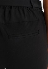 Pantalons de yoga noirs à taille élastiquée, avec une texture lisse et une petite poche arrière dotée d'une fente horizontale.