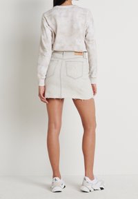 Světle hnědá tie-dye mikina spárovaná se světle šedou denimovou mini sukní. Poškozený lem a dvě zadní kapsy s koženým detailem.