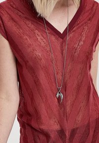 Top corto rojo, transparente, de manga corta y con cuello en V, que presenta un patrón texturizado. Un collar de plata con un colgante en forma de hoja cuelga debajo del cuello.