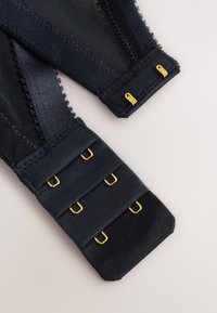 Black bra clasp showing three hooks and three corresponding eye closures with gold metal hardware on sheer fabric.