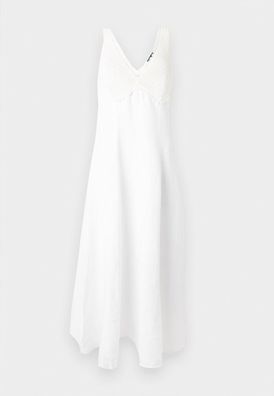 Fehér ujjatlan maxi ruha horgolt V-nyakú felsőrésszel és bővülő szoknyával, egyszínű világosszürke háttér előtt.